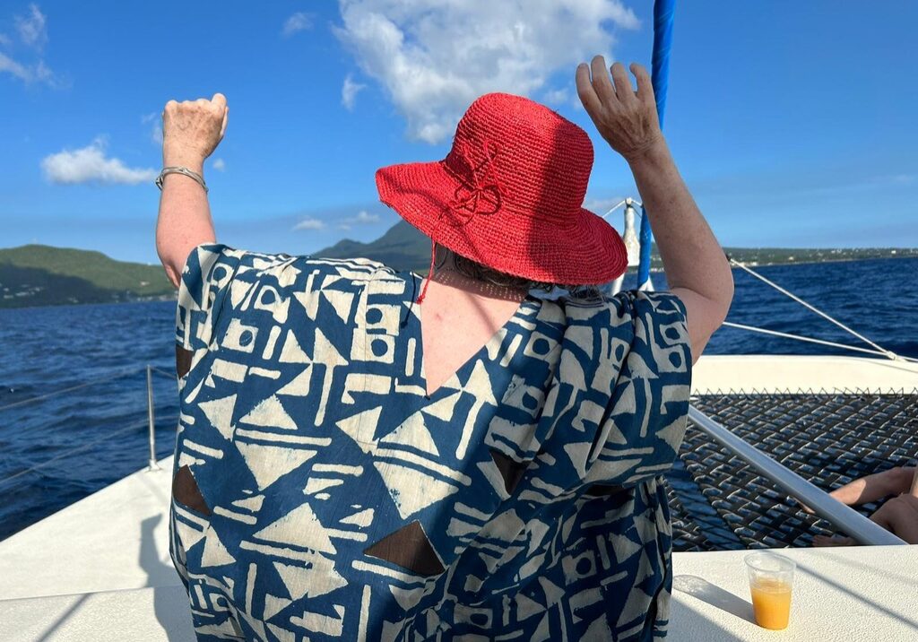 Person in a red hat raising arms on a boat under a blue sky.